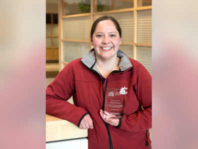 A smiling woman wearing a red Cougars jacket holding a glass award.