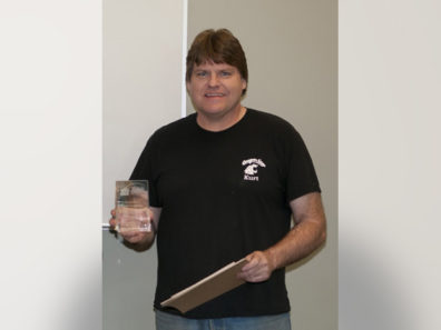 A smiling man holding a glass award.