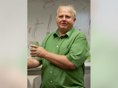 A man in a green shirt talking in front of a dry erase board.
