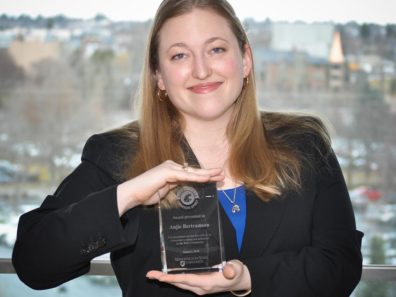 A smiling woman holding a glass award.