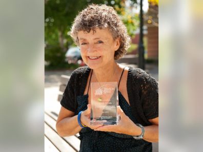 A smiling woman holding a glass award standing outside.