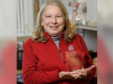 A smiling woman wearing a red shirt and holding a glass award.