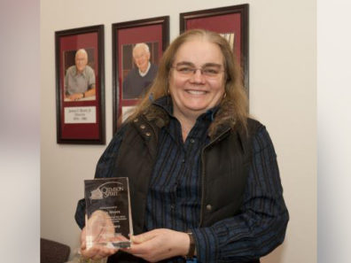 A smiling woman holding a glass award.