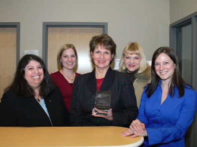 A group of smiling women and one women holding a glass award.