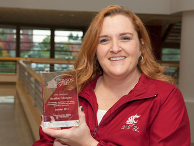 A smiling woman in a red Cougars jacket holding a glass award.