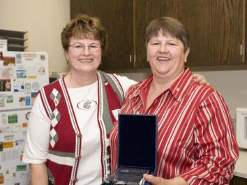 Two smiling women, one holding a box with a glass award in it.