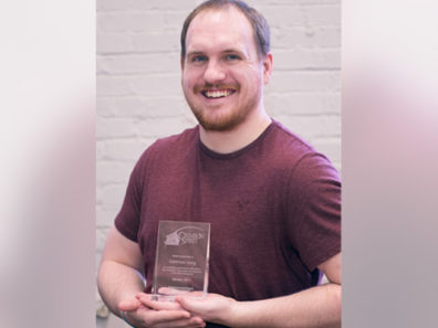 A smiling man holding a glass award.