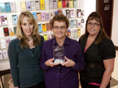 A smiling woman holding a glass award, flanked by two other women.