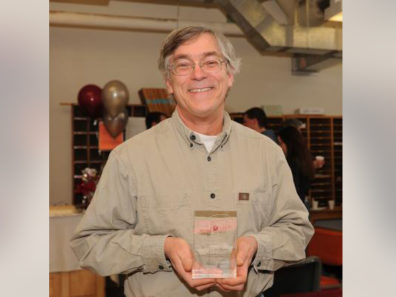 A smiling man holding a glass award.