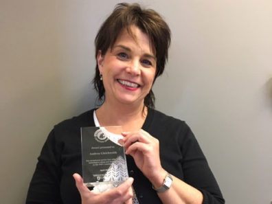 A smiling woman with short dark hair holding a glass award.