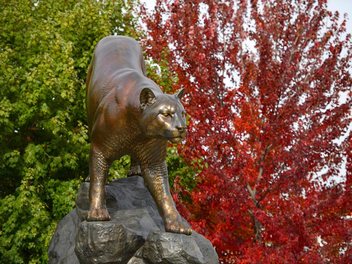 A statue of a cougar with green- and red-leaved trees.