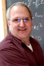 A smiling man writing math on a chalk board.