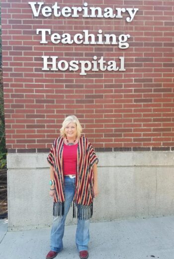 A smiling woman standing in front of a building marked with the words Veterinary Teaching Hospital.