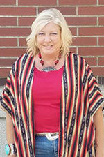 A smiling woman standing in front of a brick wall.