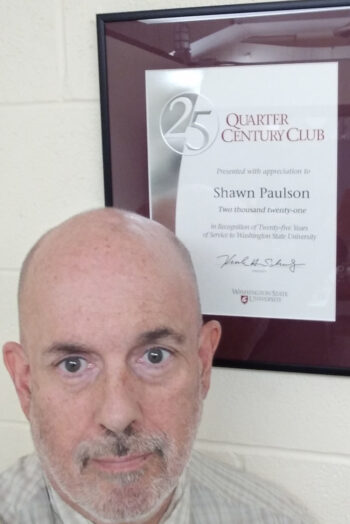 A man with a short beard next to a Quarty Century Club certificate.