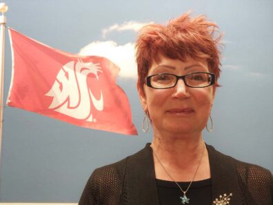 A smiling woman in front of a flag featuring the WSU cougar head.