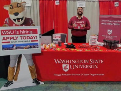 A smiling man behind a WSU hiring table.