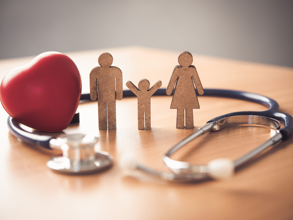 Paper cutout of a man, child, and woman, standing on a table with a stethoscope and a heart circled around them.