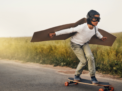 ittle boy with cardboard wings, on a skateboard, wearing an aviator cap and goggles.